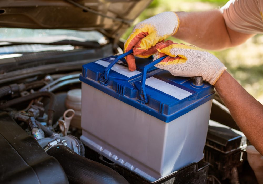 A man removes a battery from under the hood of a car. Battery replacement and repair.