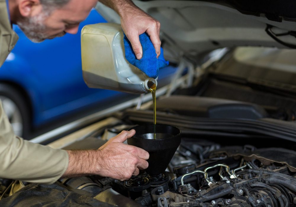 Mechanic pouring oil into car engine in repair garage